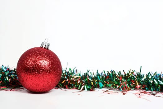 A bright red glitter ornament rests next to shiny green and red tinsel on a white surface perfect for holiday decorations.