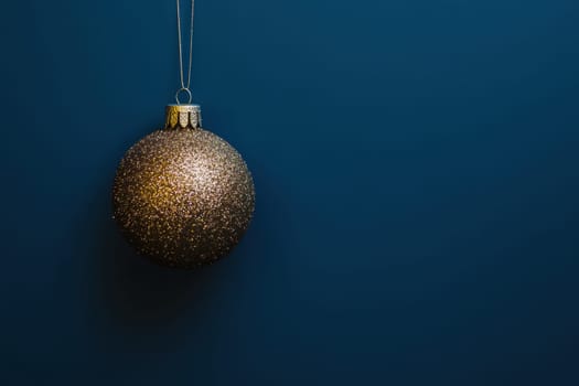 A glittering gold Christmas ornament hangs against a deep blue backdrop ready to adorn a festive holiday tree or decoration.