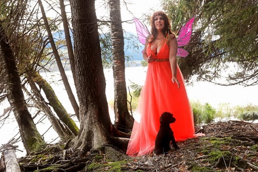 A fairy in an orange dress with wings and a little dog in the forest