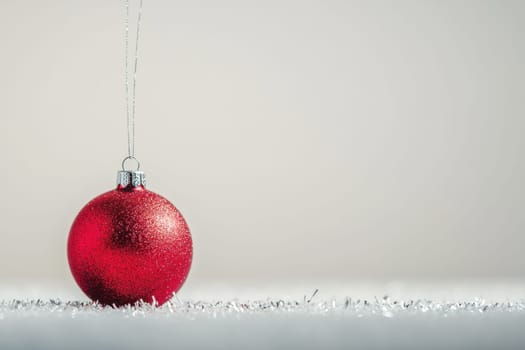 A vibrant red ornament hangs delicately catching light against a soft neutral background creating a festive holiday ambiance.