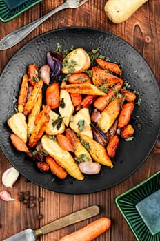 Roasted root vegetables, baked parsnip root, red onions, carrots, and garlic for a vegan dish.