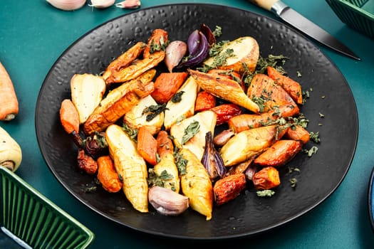 Roasted root vegetables, baked parsnip root, red onions, carrots, and garlic for a vegan dish.
