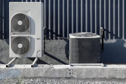 Two different types of outdoor air conditioning units are installed outside a building, showcasing the benefits of modern cooling technology at sunny day