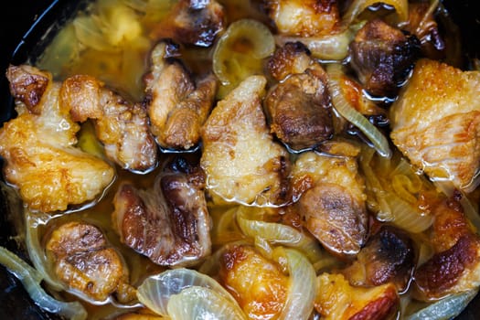 roasted pork meat with onion rings submerged in a vegetable oil, closeup full-frame background