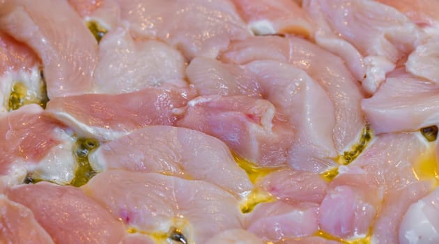 closeup full-frame background of raw chicken breast meat just starting to roast.