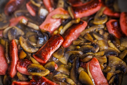 closeup view of roasting cut champignon mushrooms and sausages.