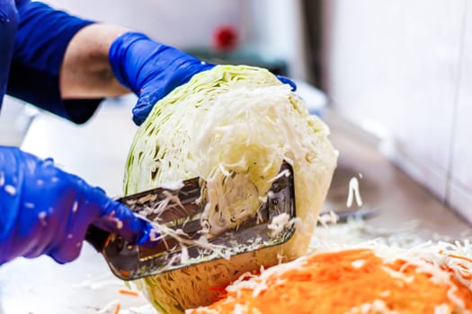 hands in blue gloves cutting cabbage with special double blade slit cabbage shredder knife during sauerkraut preparation
