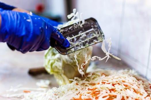 hands in blue gloves cutting cabbage with special double blade slit cabbage shredder knife during sauerkraut preparation