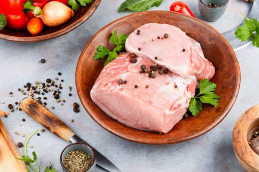 Raw pork loin chops for grill, barbecue or cooking with spices and vegetables on wooden background. Rustic style.