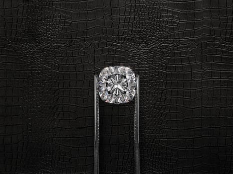 Cut Beautiful diamond held by tweezers, on a black leather background