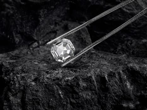 Cut Beautiful diamond held by tweezers on black coal background