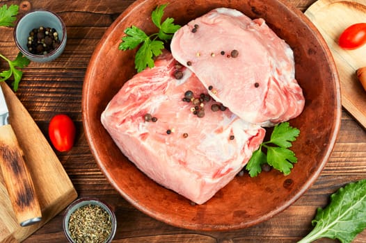 Raw pork loin chops for grill, barbecue or cooking with spices and vegetables on wooden background. Rustic style.
