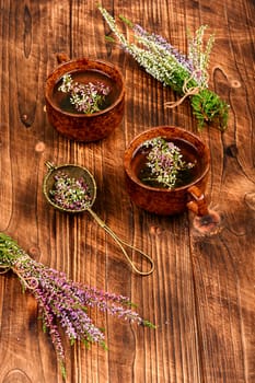 Heather herbal tea in a glass mug and forest herbs on a table. Tea from autumn herbs. Phytotea.