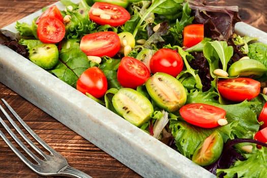 Homemade vegetarian salad with greens, colorful cherry tomatoes on a stylish stone tray. Vegan meal. Flat lay