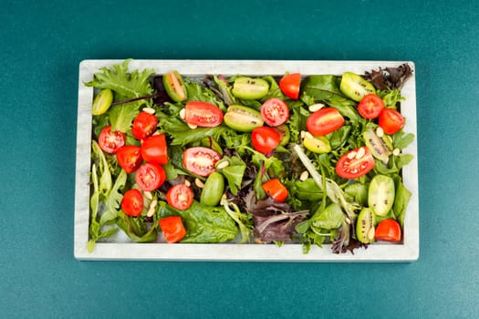 Homemade vegetarian salad with greens, colorful cherry tomatoes on a stylish stone tray. Vegan meal. Flat lay
