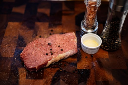 Raw meat steak with seasonings on wooden cutting board.