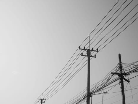 Black and white photo of Reinforced concrete pillar with high-voltage wires against a clear sky. Transmission of electricity by wires over long distances. Electricity power lines against a clear sky.