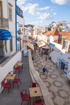 Albufeira, Portugal - April 27, 2024: traditional buildings and tourists photographed in a street of  Albufeira at the Algarve coast of Portugal