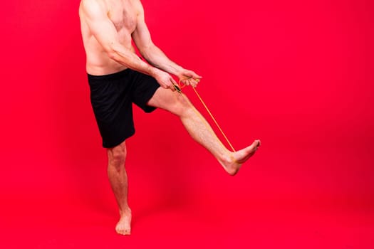 Fit man jumping with skipping rope. Isolated on a red studio background