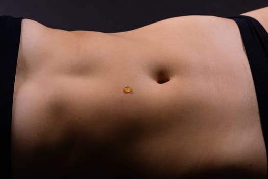 Beautiful seductive young female makes honey on a black background. Drops of honey on her belly.