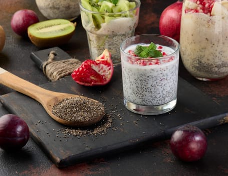 A glass with chia seeds and yogurt, pomegranate seeds are added to the dessert. A wooden spoon is nearby