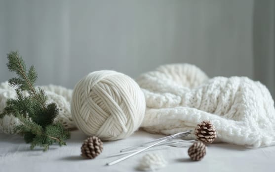White yarn ball with knitting needles, pine cones, and evergreen branches on soft fabric, evoking a serene winter crafting atmosphere.