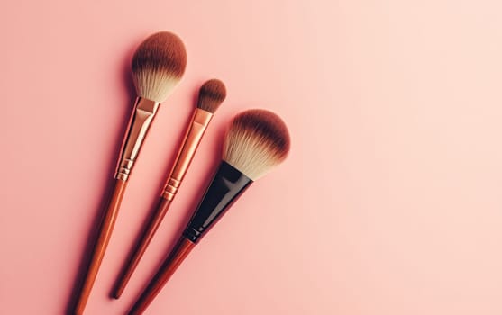 Set of three high quality makeup brushes with wooden handles and soft bristles arranged on a pastel pink background with copy space.