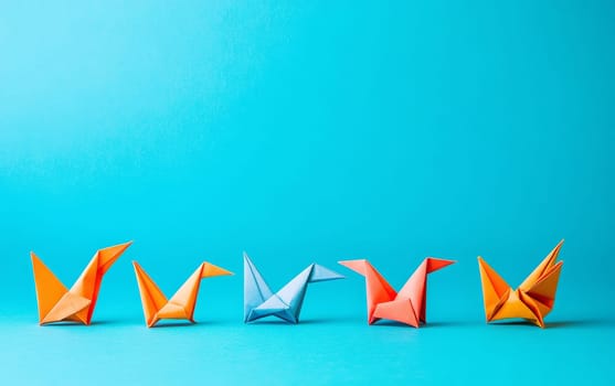 Row of vibrant origami birds in orange, blue, and pink on bright turquoise background. Concept of diversity, creativity, and teamwork with copy space.