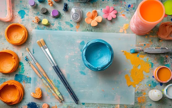 Messy artist workspace with colorful acrylic paints, brushes, and decorative elements on light blue background, inspiring creativity and artistic expression.