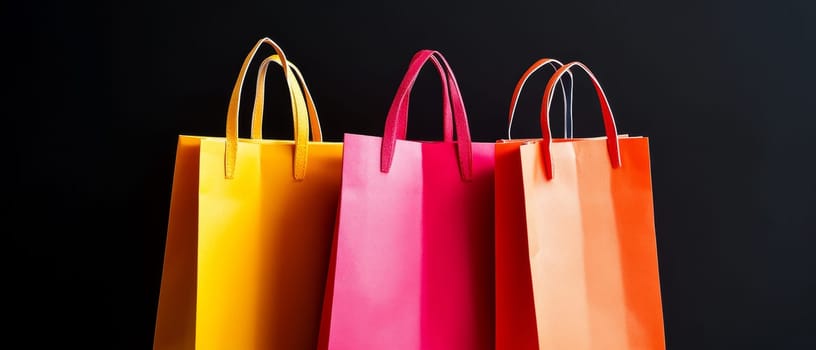 Vibrant shopping bags in yellow, pink, and orange against a black backdrop, representing retail and fashion. Black Friday sale concept with place for text.