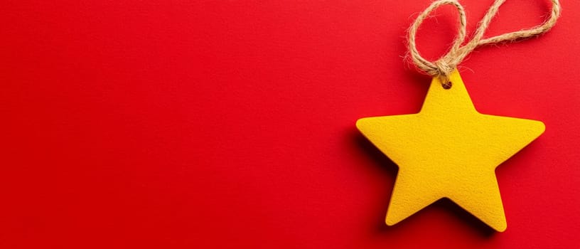 Bright yellow star ornament with a twine loop on a vibrant red background, featuring copy space for text.