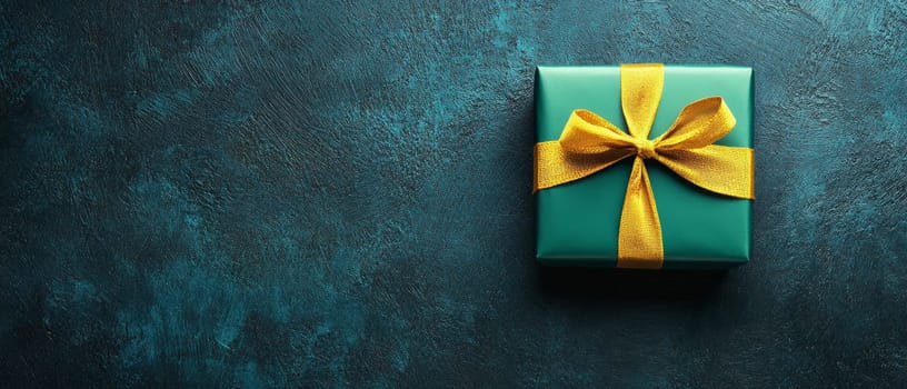 Elegant gift box wrapped in teal paper with a golden ribbon, set against a textured blue background with copy space.