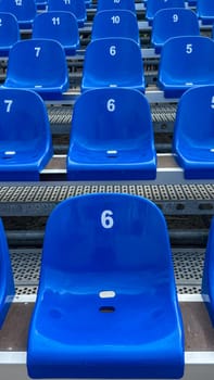Close-up of blue plastic stadium seats, each marked with a white number. Focus on seat number 6. The organized rows create a repeating pattern, structure, and simplicity.