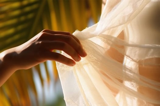 young long-haired curly woman in a white dress. straightens a light white transparent fabric with his hand on a sunny day. against the backdrop of a palm tree