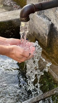 Hands under a stream of water from a metal outdoor faucet pouring into a stone bowl. freshness and nature.