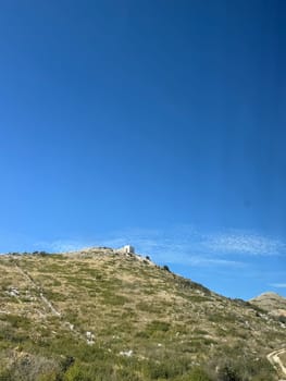 Grassy hill with a white house on it under a clear blue sky with minimal clouds.