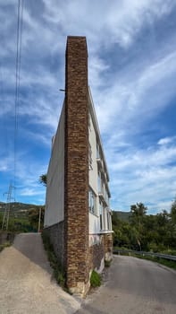Unique irregular shaped building stands tall under blue sky, located between two roads. Narrow design with open landscape behind it.Budva, Montenegro.26.09.24. High quality photo