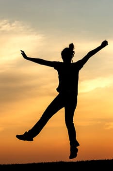 Silhouette of teen girl jumping for joy at sunset.