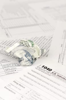 1040 Individual income tax return form and crumpled hundred dollar bill. Loss of money to pay taxes concept