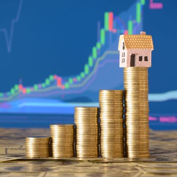 Small toy house model and coins stacks in growth graph. Planning savings money of coins to buy a home concept, mortgage and real estate investment