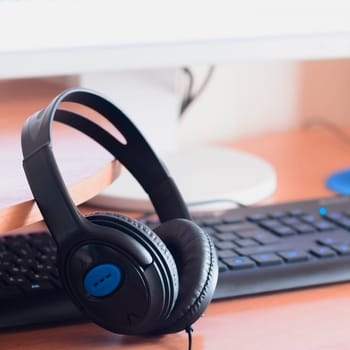 Big black headphones lie on the wooden desktop of the sound designer. Workplace for music creator. Selective focus