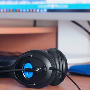 Big black headphones lie on the wooden desktop of the sound designer. Workplace for music creator. Selective focus