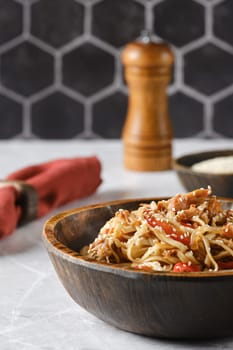 A flavorful dish of stir-fried noodles with colorful vegetables is presented in a rustic wooden bowl. The backdrop features a stylish hexagonal tile pattern, creating a cozy atmosphere.