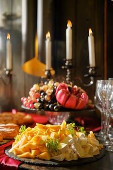 A beautifully arranged cheese platter features an assortment of cheeses alongside a colorful fruit display. Elegant candles illuminate the table, creating a warm atmosphere perfect for a gathering.