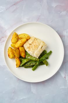 A perfectly cooked cod fillet on a white plate, accompanied by savoury roasted potatoes and vibrant green beans, showcasing a well-balanced and healthy meal presentation ideal for dinner.