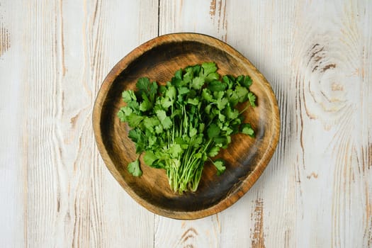 A vibrant bunch of freshly picked cilantro on a rustic wooden plate, showcasing its rich green color against a textured light wooden table, perfect for culinary use.
