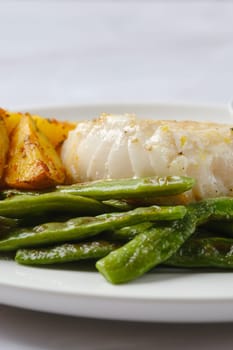 A plate showcases tender white fish alongside perfectly roasted golden potatoes and vibrant green beans. The dish highlights fresh ingredients, ideal for a nutritious and satisfying meal.