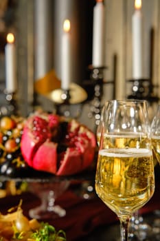 A beautifully arranged table features sparkling champagne flutes and a vibrant array of seasonal fruits, including pomegranate, all illuminated by soft candlelight for a festive vibe.
