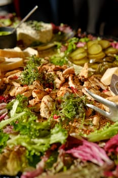 A colorful array of fresh ingredients features grilled chicken pieces, assorted leafy greens, and pickles, delighting guests at a lively event.