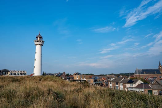 The approx. 28 m high white lighthouse J.C.J. van Speijk in Egmond aan Zee, North Holland, Netherlands with some of the town's houses with dune grass